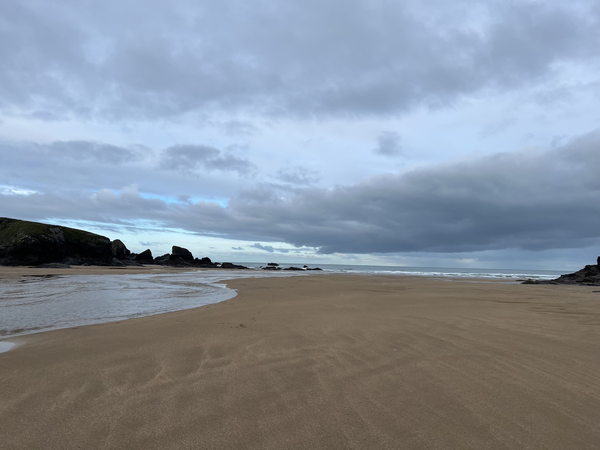 Sandy beach with shadowy cliffs and cloudy sky