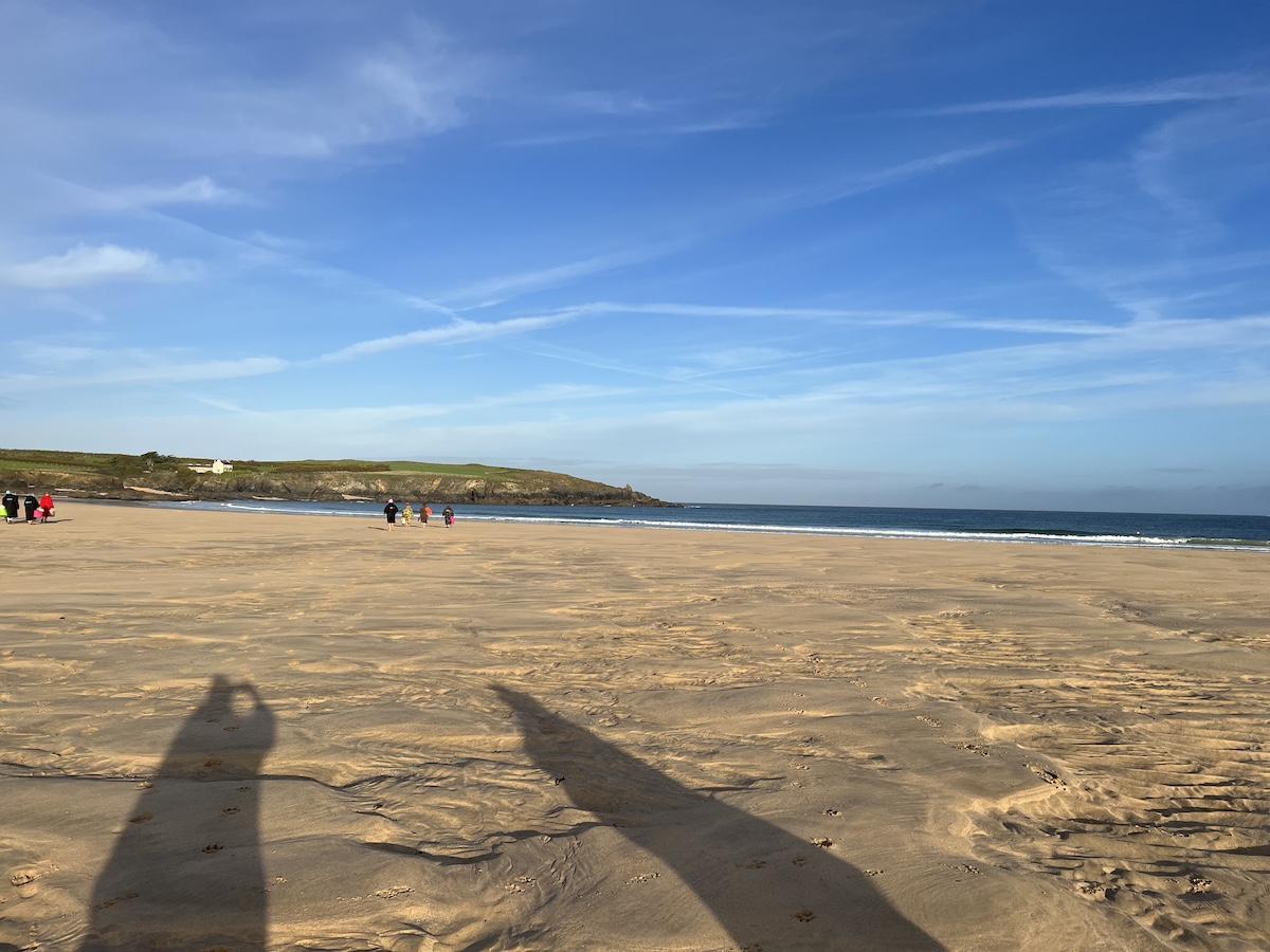 Sandy beach with two people shadows and cliff tops in the distance