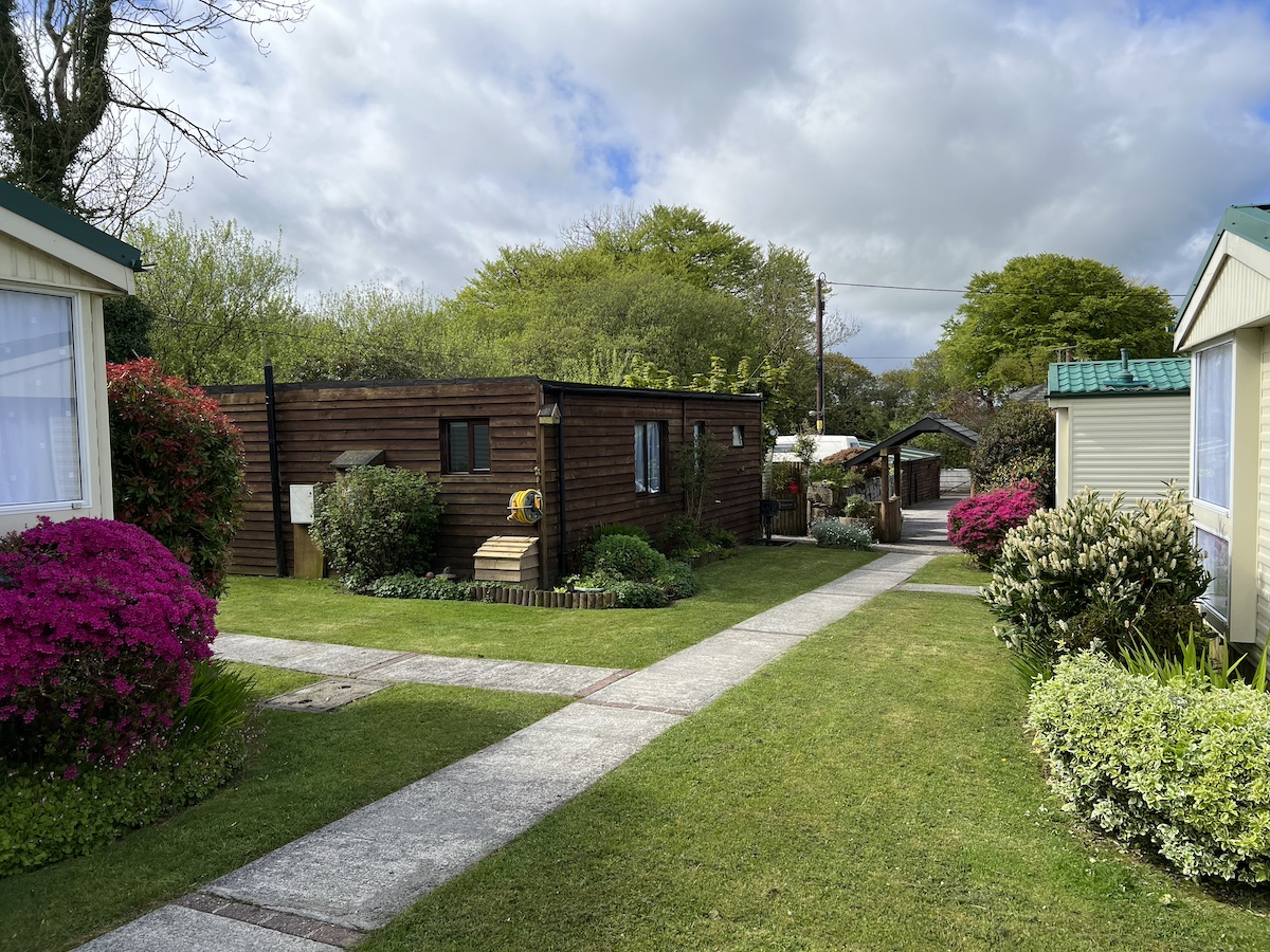 Wooden chalet surrounded by grass, concrete pathway and caravans