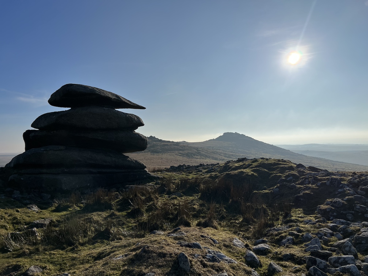 Stacked granite rocks on top of moorland with blue sky and sunshine in the background