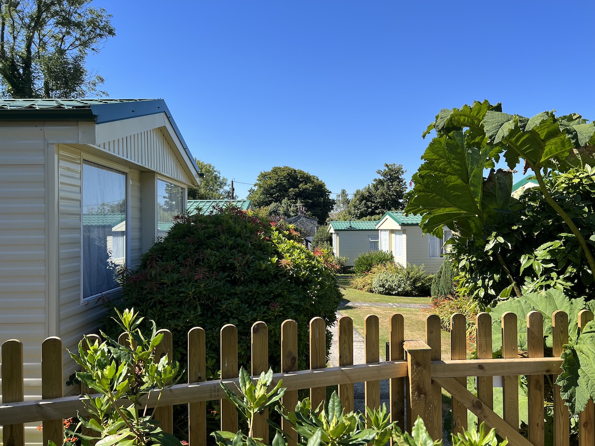 Wooden picket fence and plants/bushes in front of a cream caravan with other caravans in the background