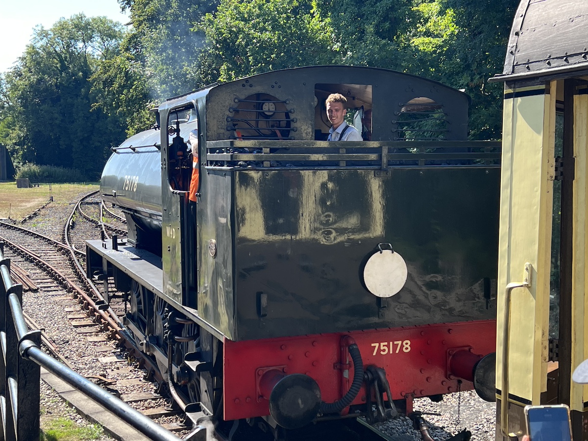 Black steam engine on railway track with a smiling train driver