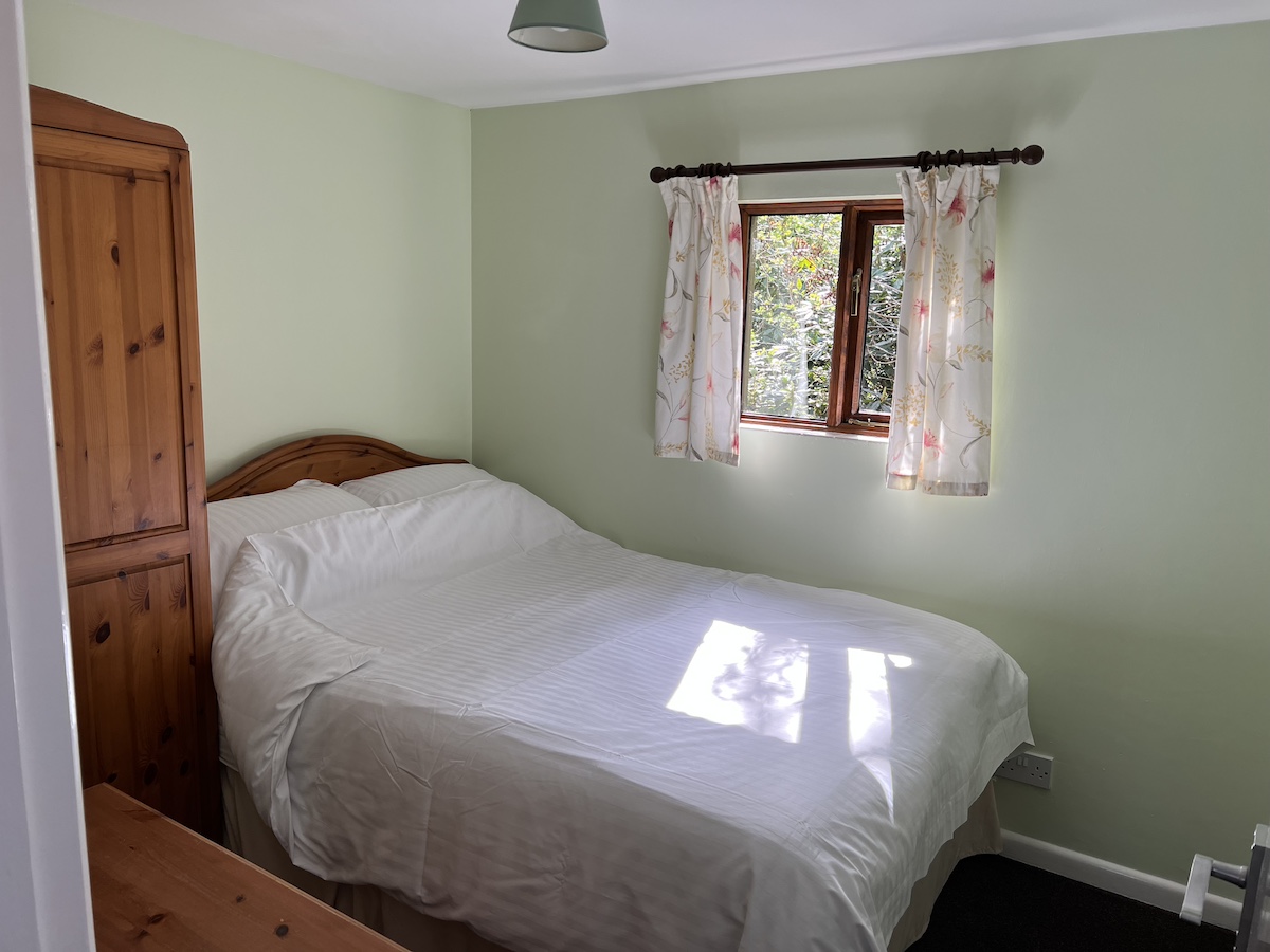 Bedroom with double bed, wooden wardrobe and drawers, pale green walls and window