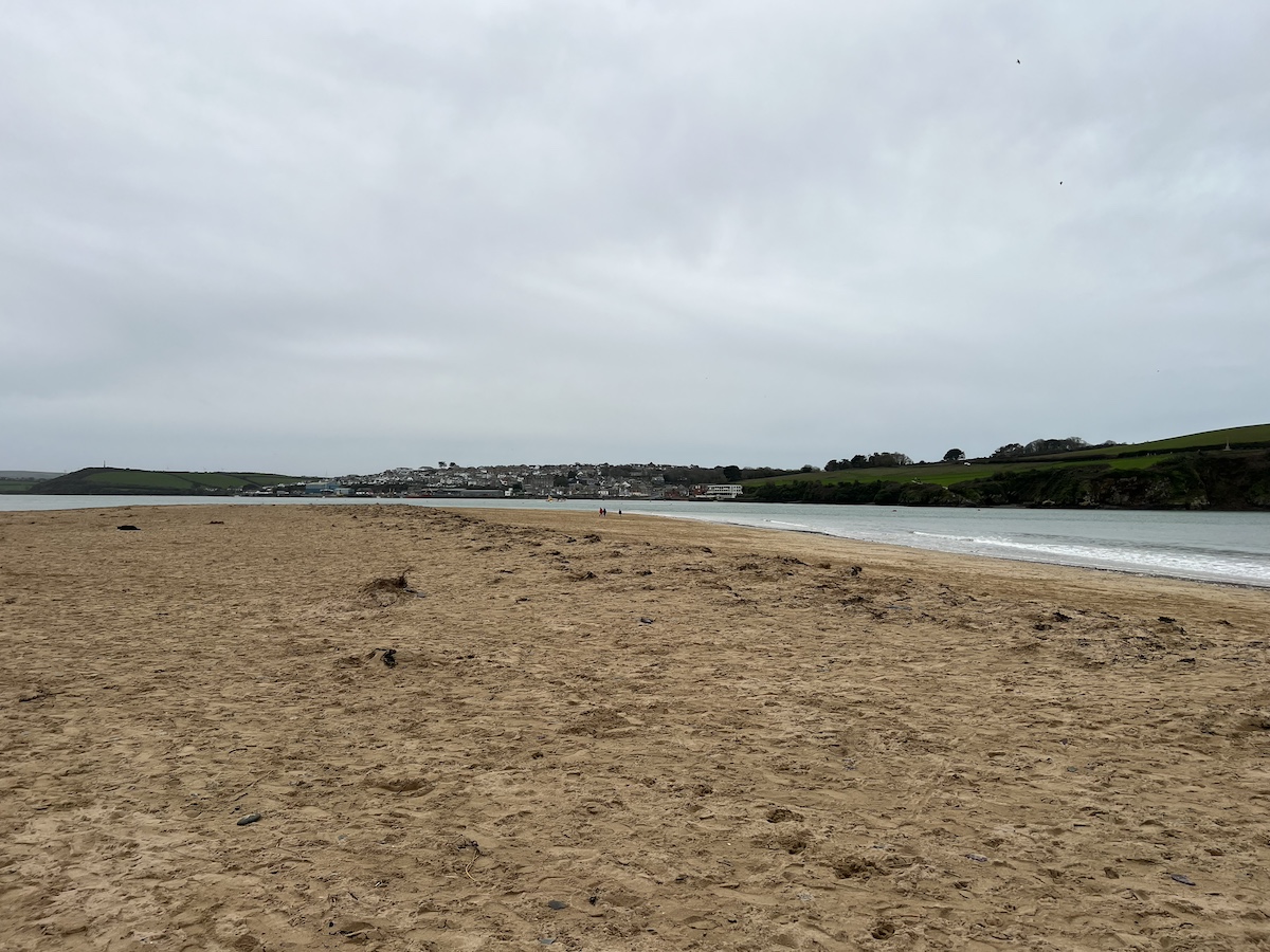 Sandy beach with grey cloudy sky and Padstow in the background