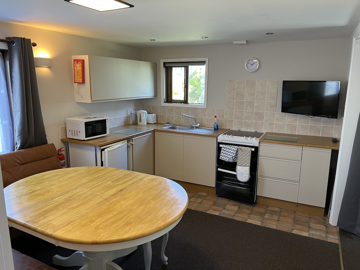 Kitchen / dining area with wooden dining table, cream and wood kitchen floor and wall units, windows and television on wall