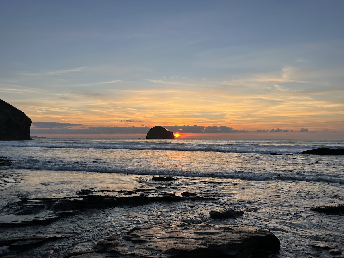 Beach and sea with rock, blue sky and setting sun in the background