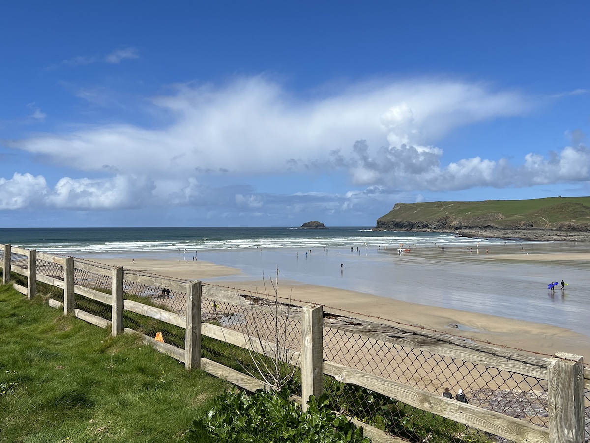 Wooden fence in front of a wide expanse of beach and cliff in the background