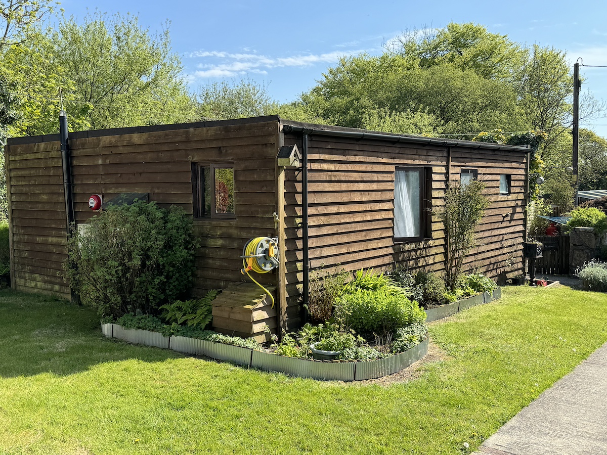 Wooden chalet surrounded by grass and plants with trees in the background