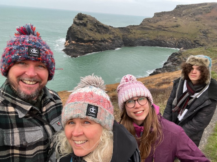 Four people wearing winter hats, standing on a cliff top by the sea