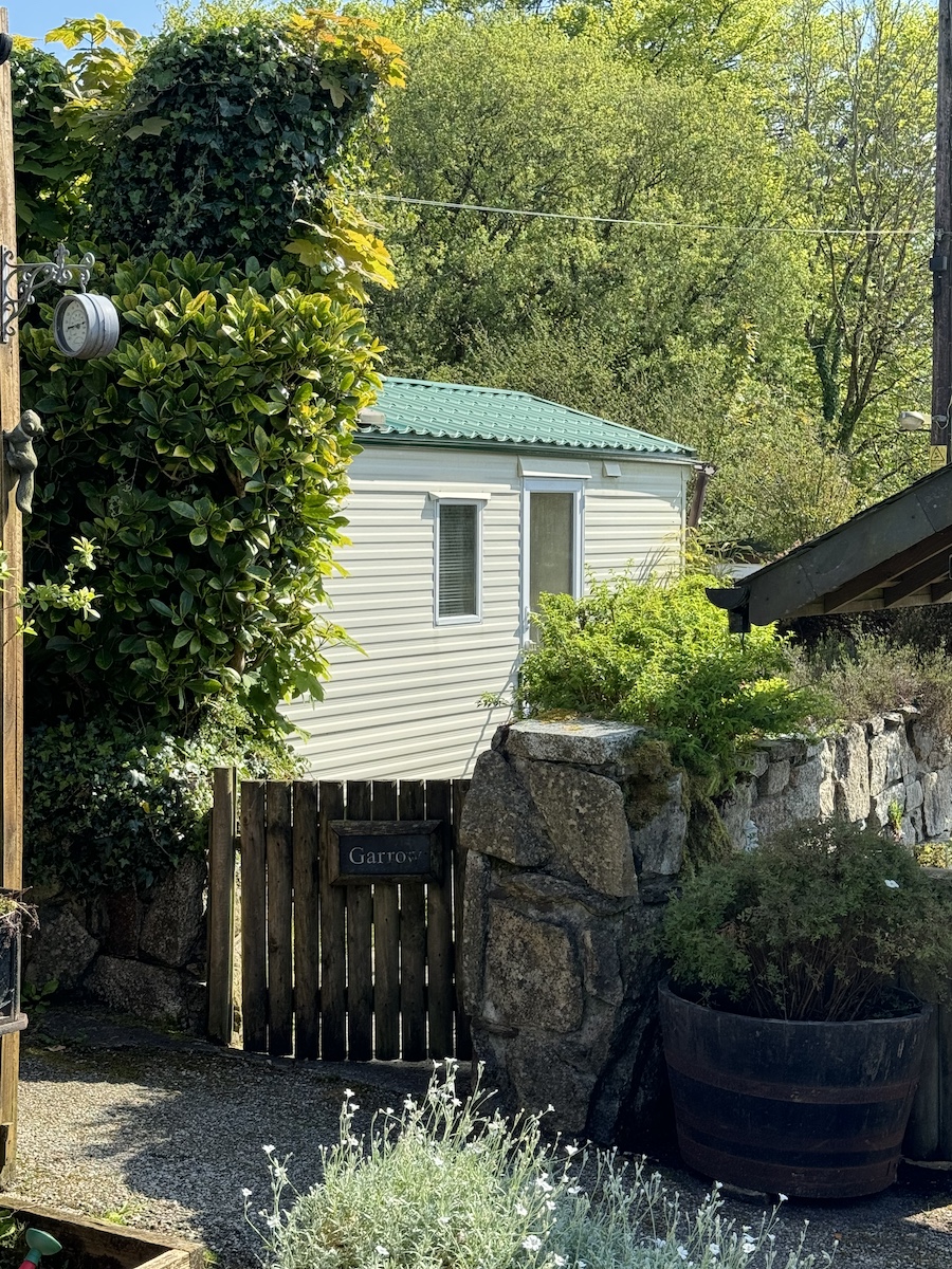 Cream caravan with green roof, surrounded by trees, wall and wooden gate