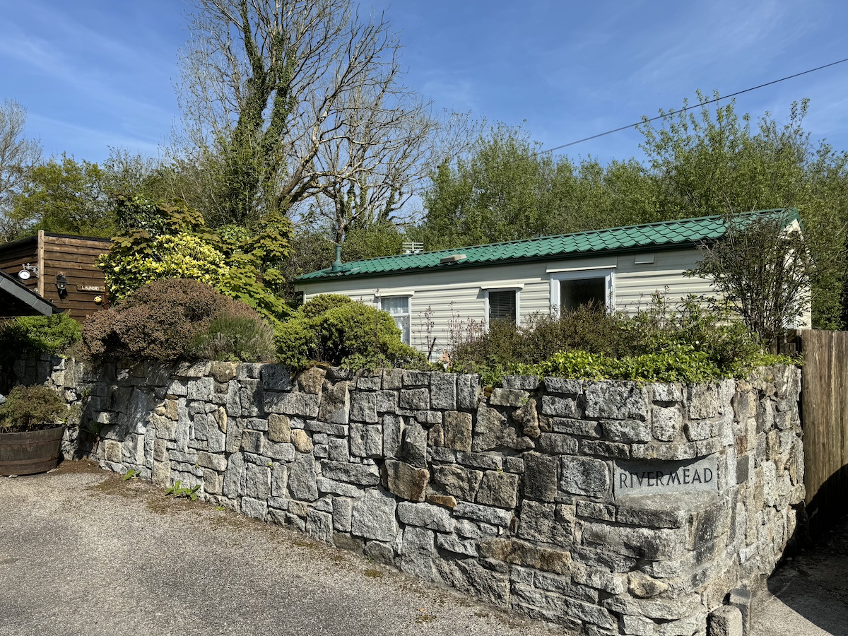 Cream caravan with green roof, surrounded by stone wall and trees