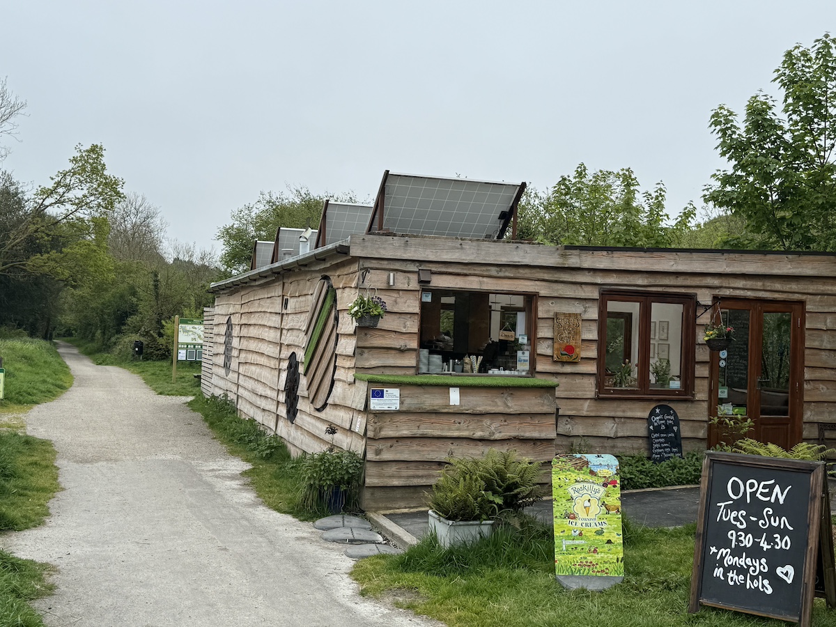 Wood-clad building with solar panels on roof and chalkboard sign that says "Open Tues-Sun 9.30-4.30 *Mondays in the hols"