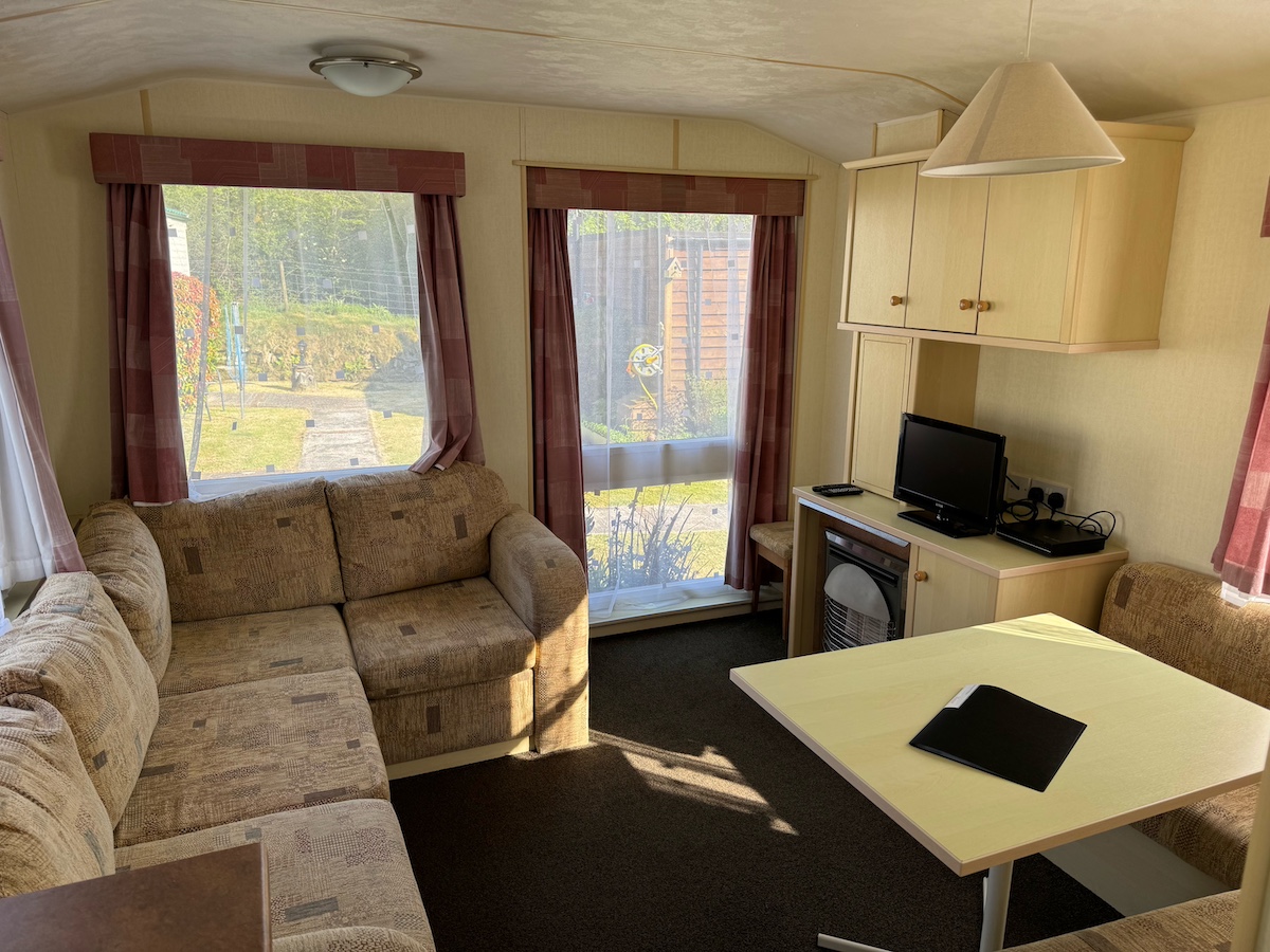 Caravan living room with settees, table, cupboards, television and windows