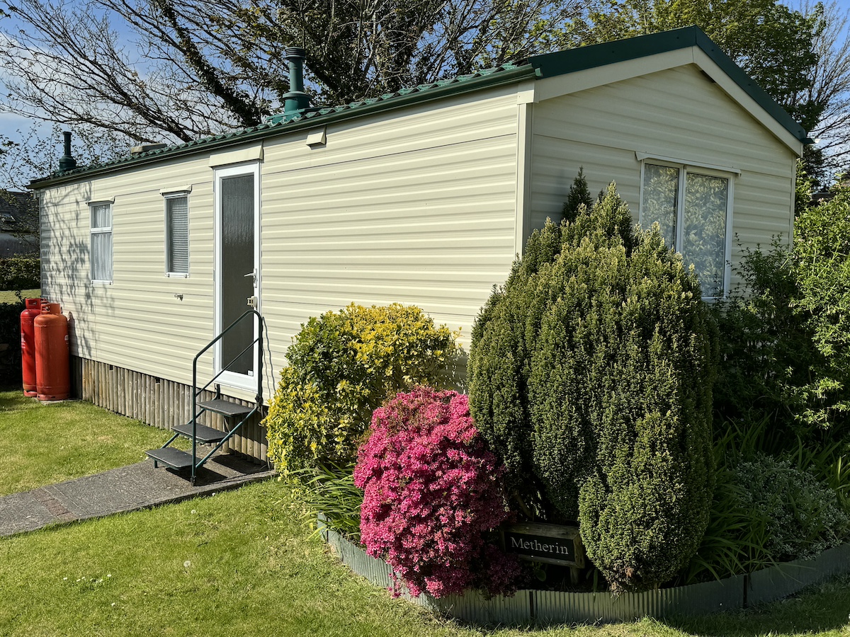 Cream caravan with green roof, surrounded by trees and bushes