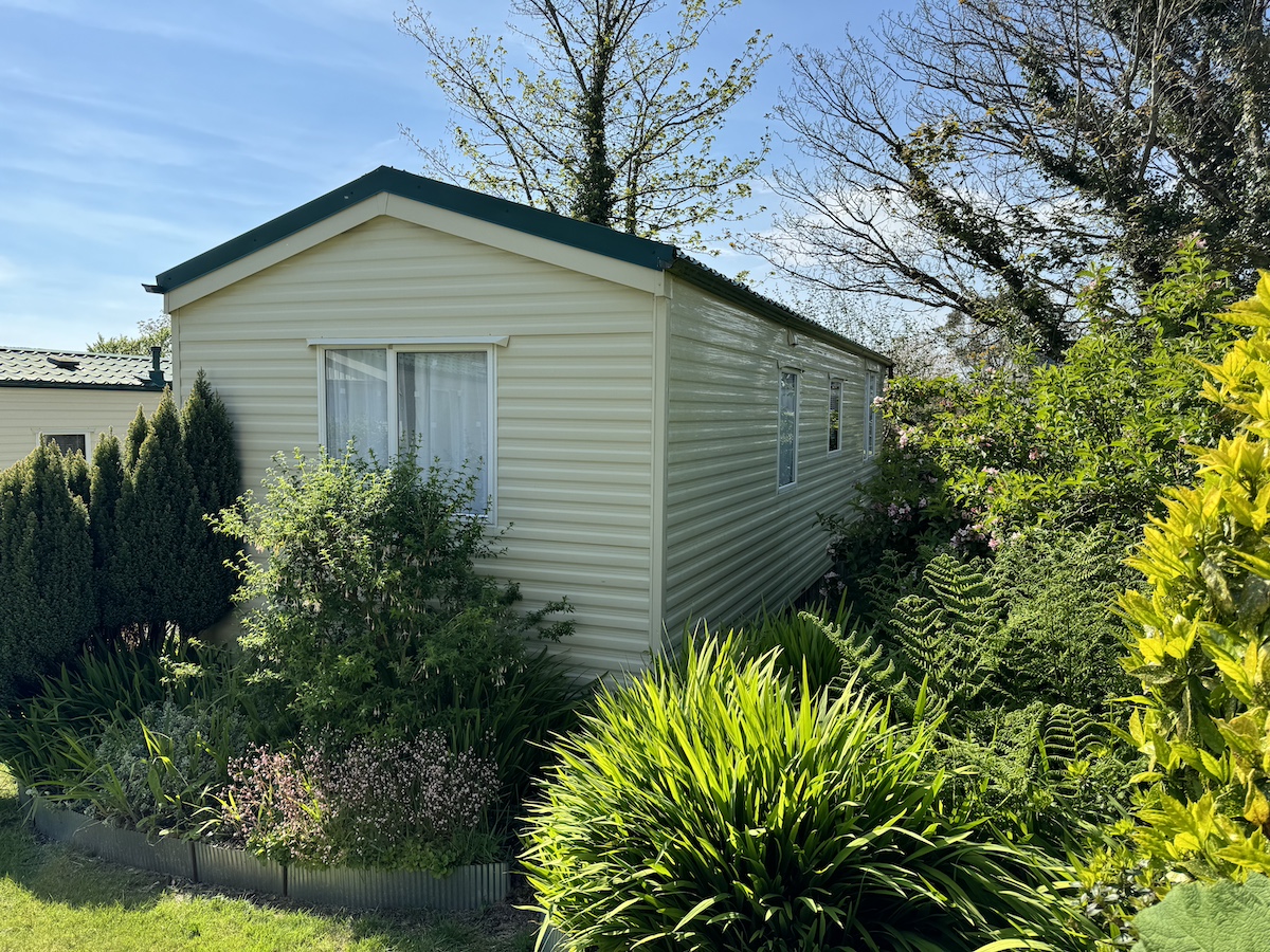 Cream caravan with green roof, surrounded by trees and bushes
